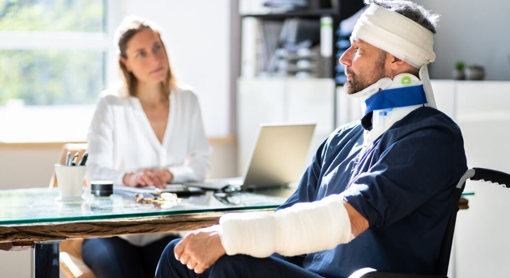 injury man with neck brace, an arm cast, head wrap, and in a wheelchair meeting with a woman